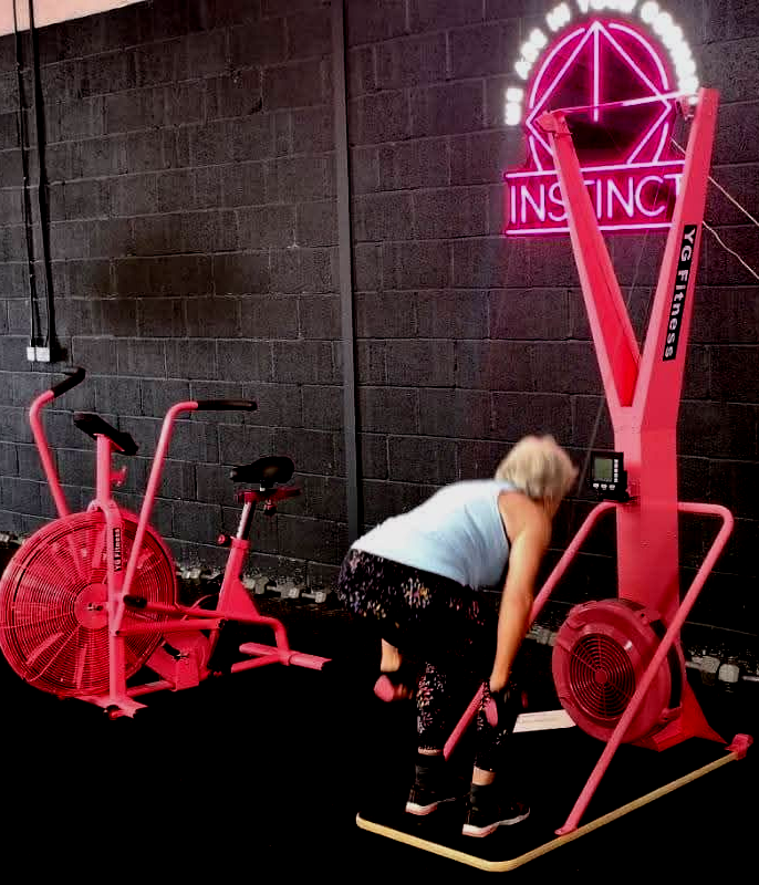 Person using a bright pink exercise machine in a gym with neon “INSANE” sign