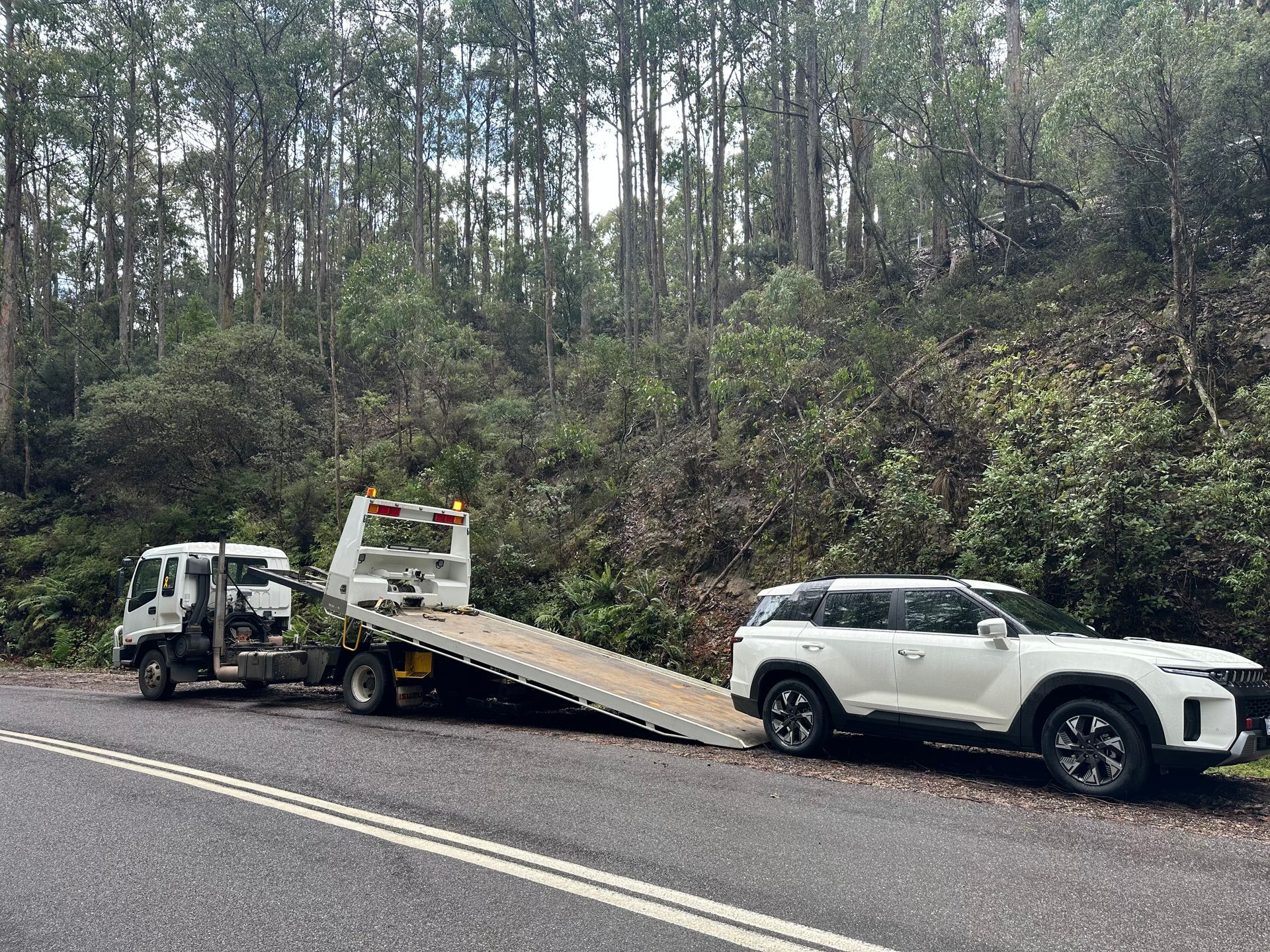 Tow Truck Hauling a White SUV on a Road Beside a Wooded Hillside — Connect Trailers and Towing Pty Ltd In Prospect Vale, TAS
