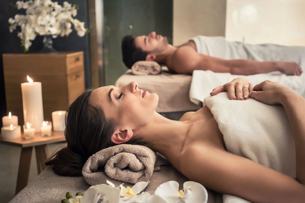 Two people receiving relaxing spa massages with candles and white towels in a dim room