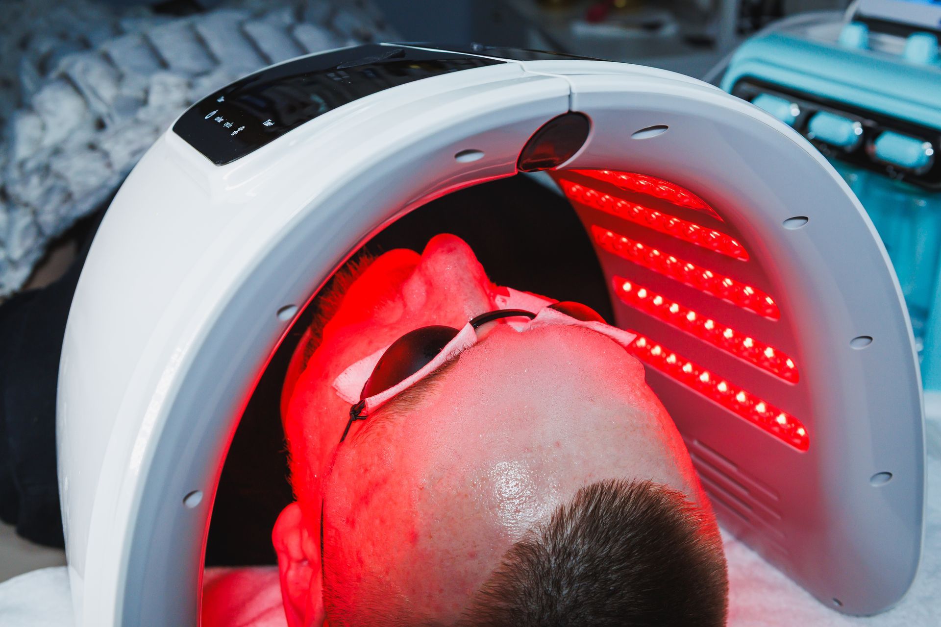Person under a red LED light therapy mask, lying back with the device covering their face