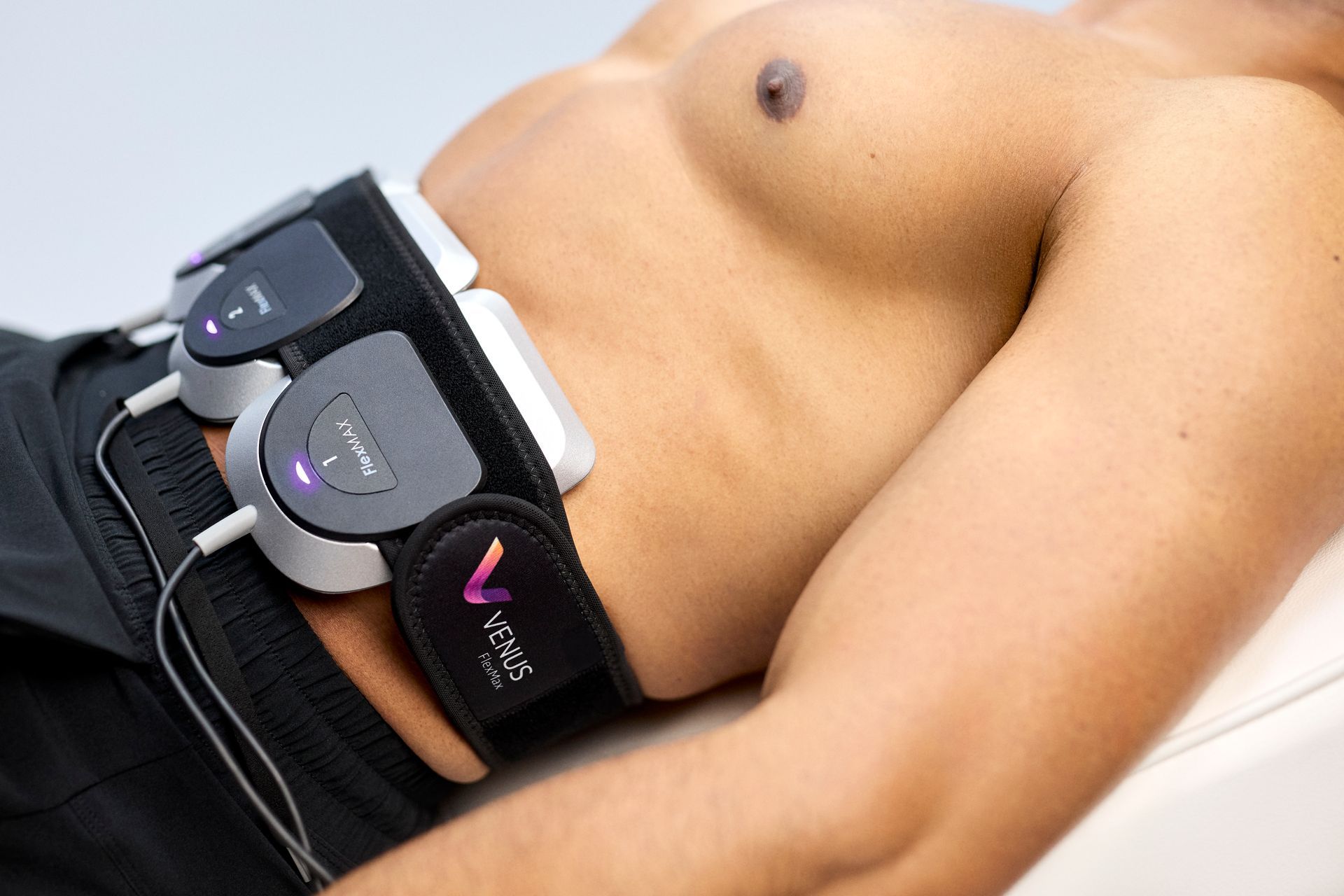 A person wearing a black belt device on their lower back and hips, shown lying on a white surface.