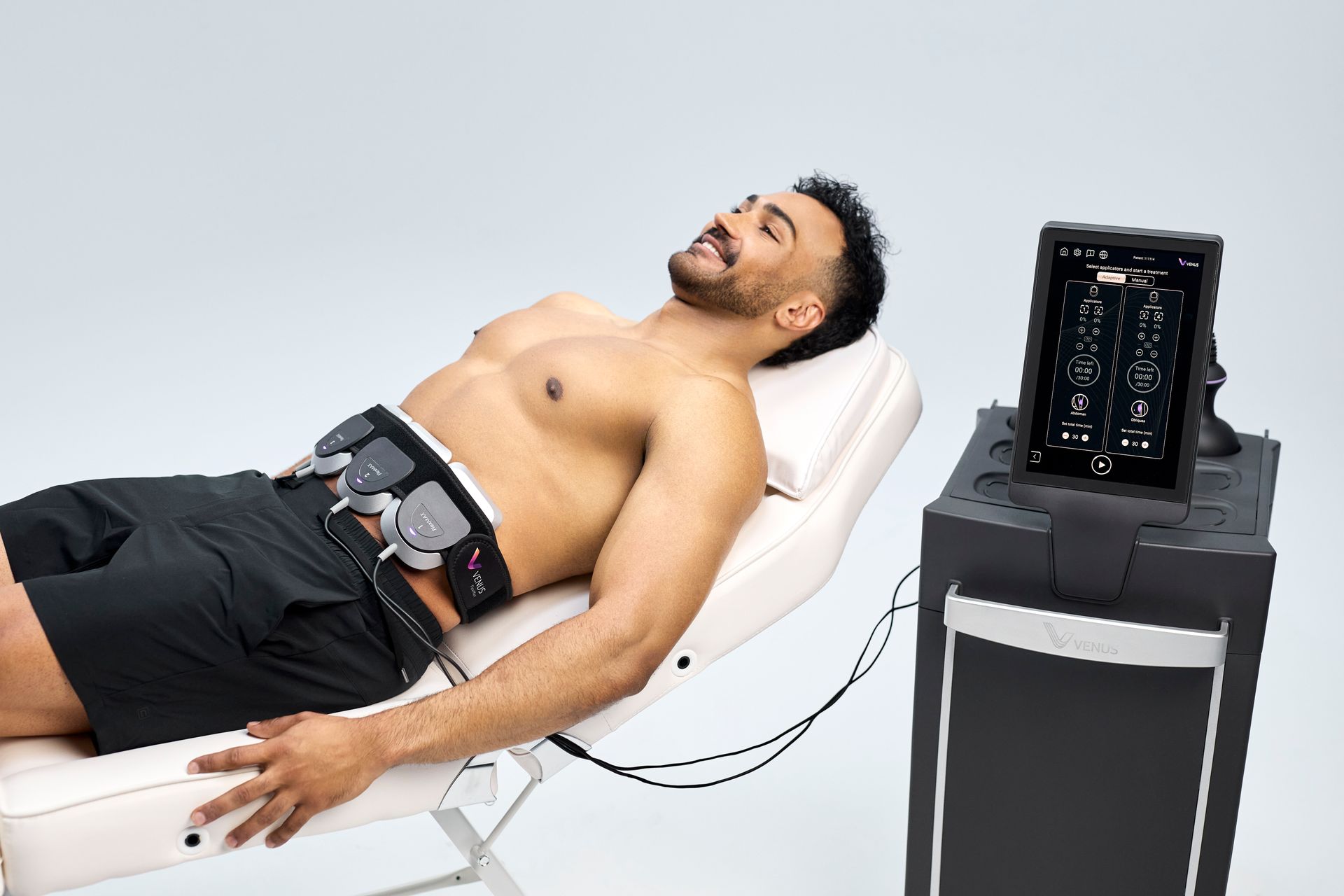 Man lying on a reclined exam chair with sensors on his torso beside a medical monitor