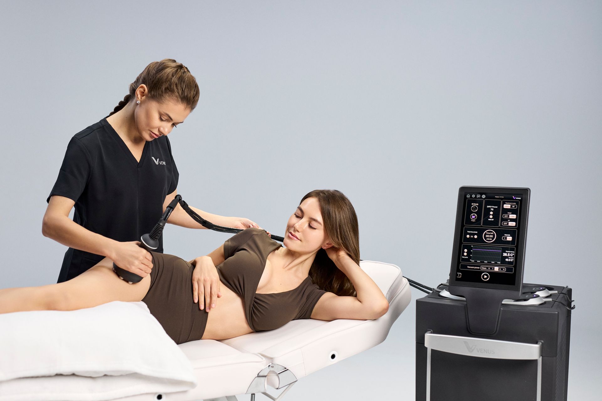Physical therapist adjusting a reclining woman's leg beside a portable ultrasound machine
