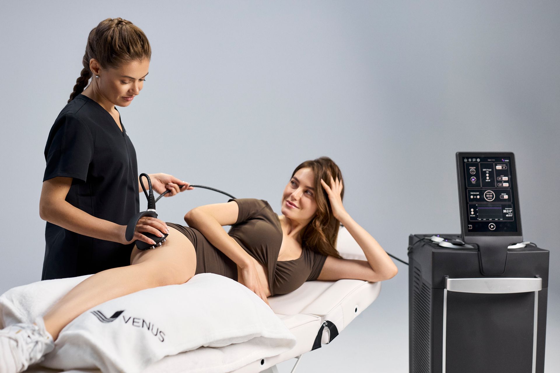 Therapist using a handheld device on a patient reclining on a treatment table beside a medical monitor
