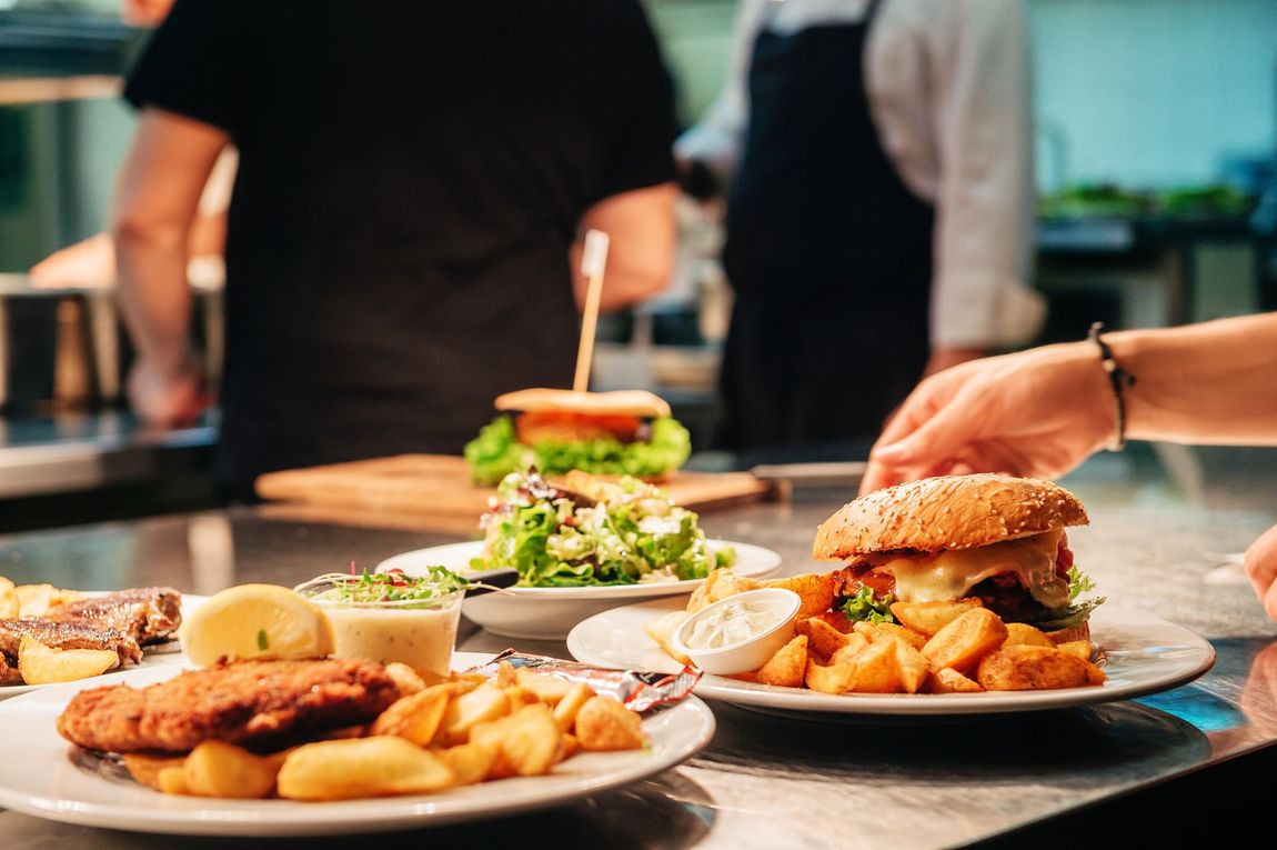 Plates of burgers and fries on a restaurant table, with a hand serving a burger in the foreground.