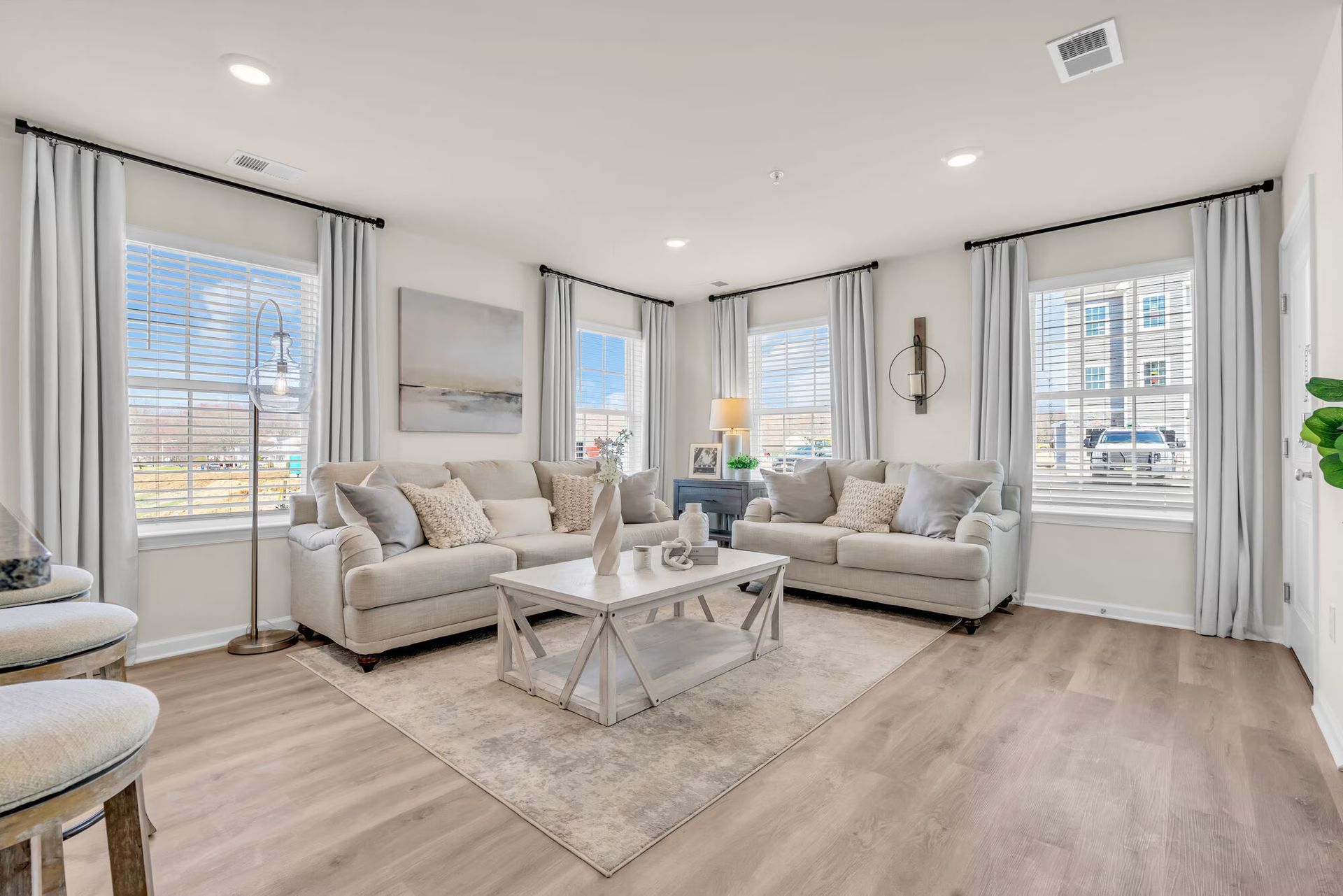 Bright living room with light gray sofas, white coffee table, large windows, and beige wood floors