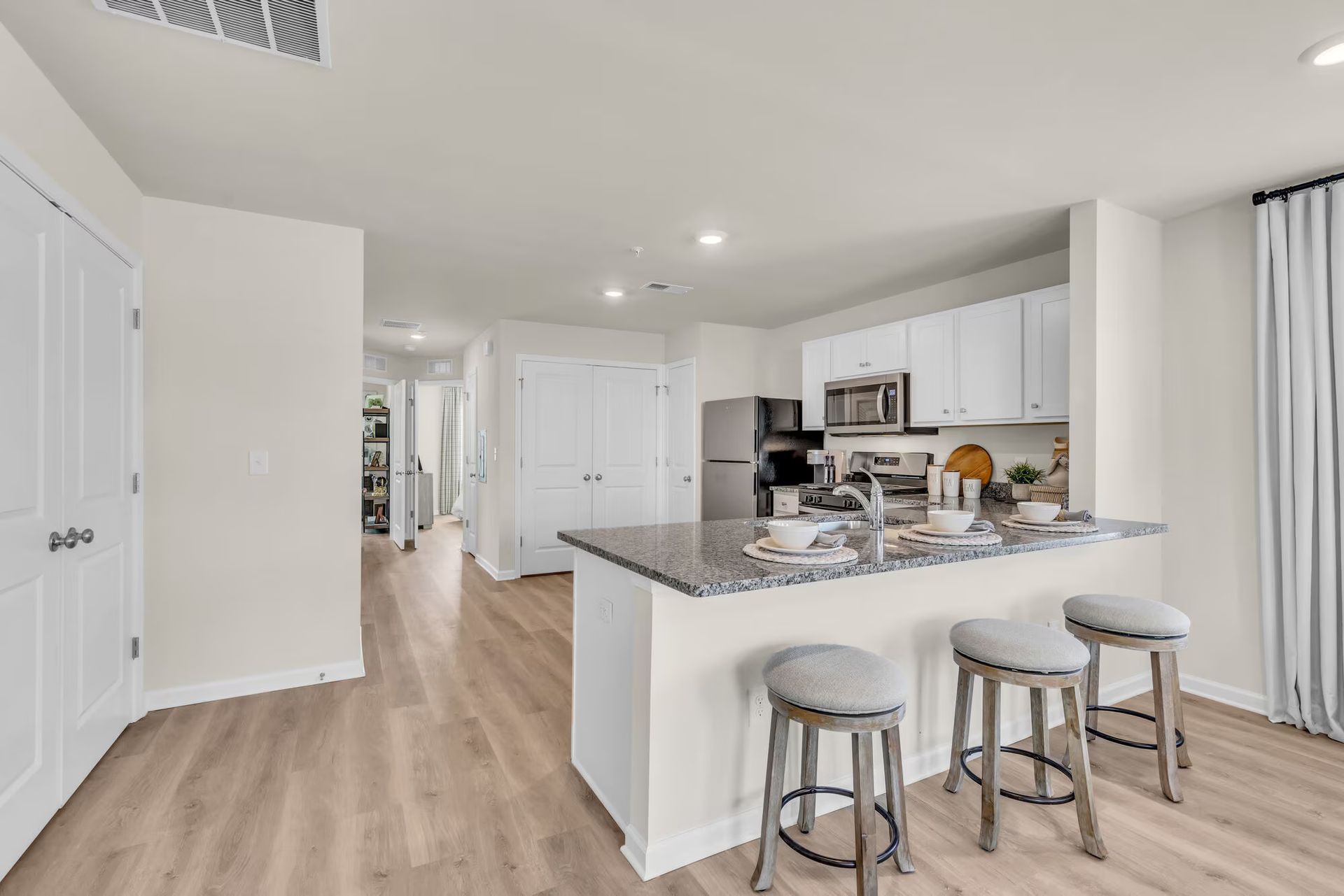 Bright modern kitchen with white cabinets, gray island, and three stools in an open living space