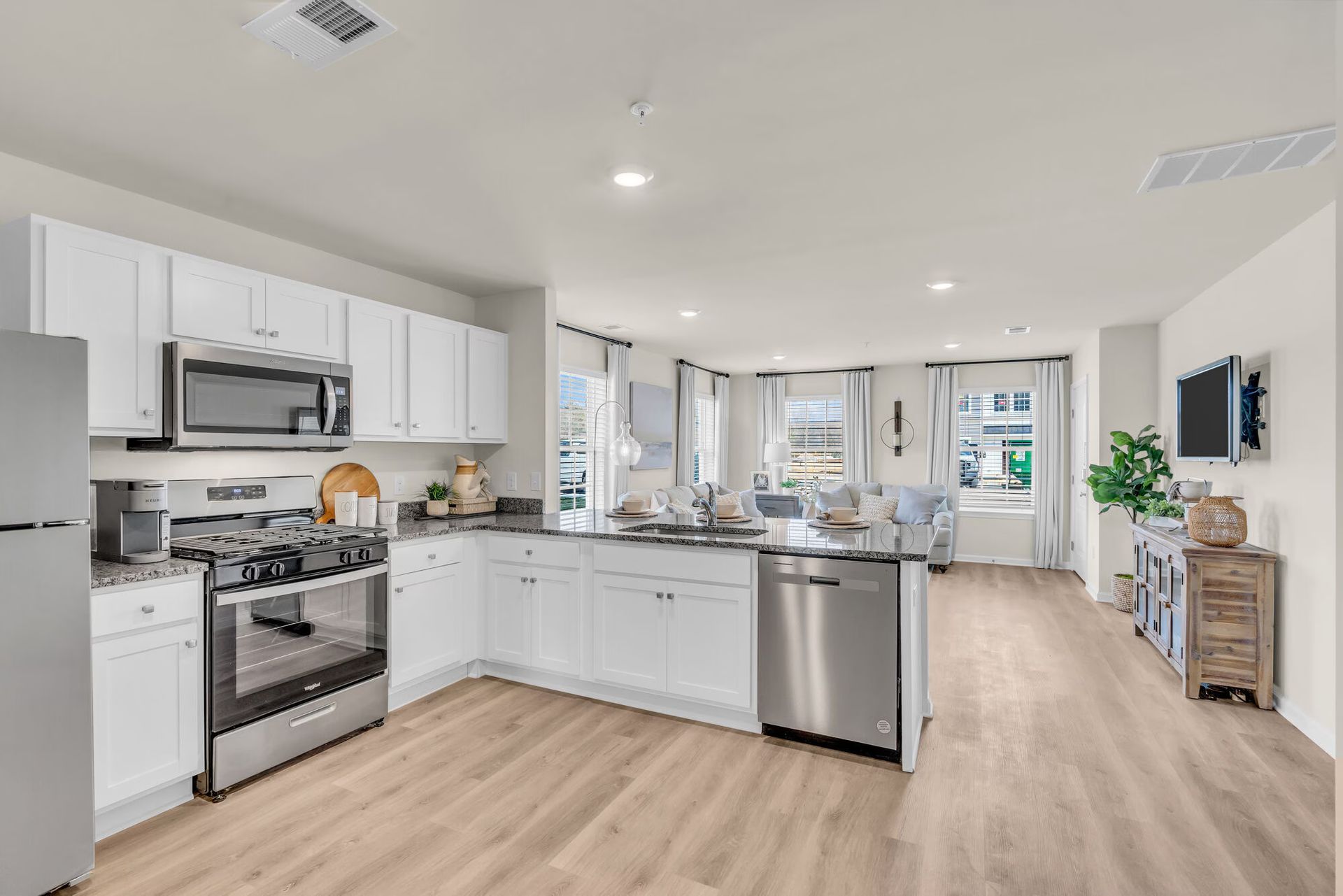 Bright modern kitchen with white cabinets, stainless appliances, island, and open living area.