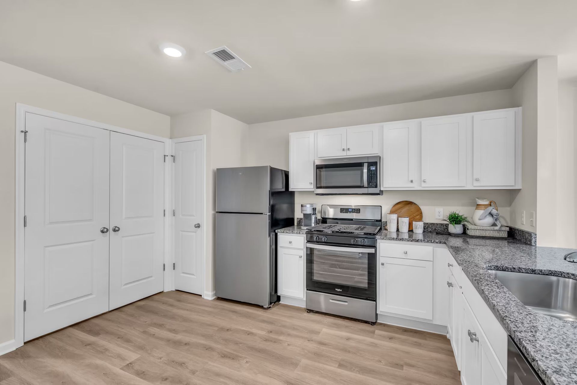 Modern white kitchen with stainless steel appliances, granite counters, and light wood flooring