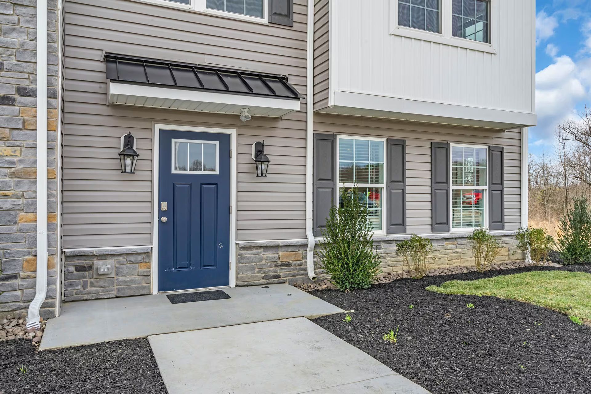 Front entry of a house with a blue door, stone accents, and a concrete walkway.