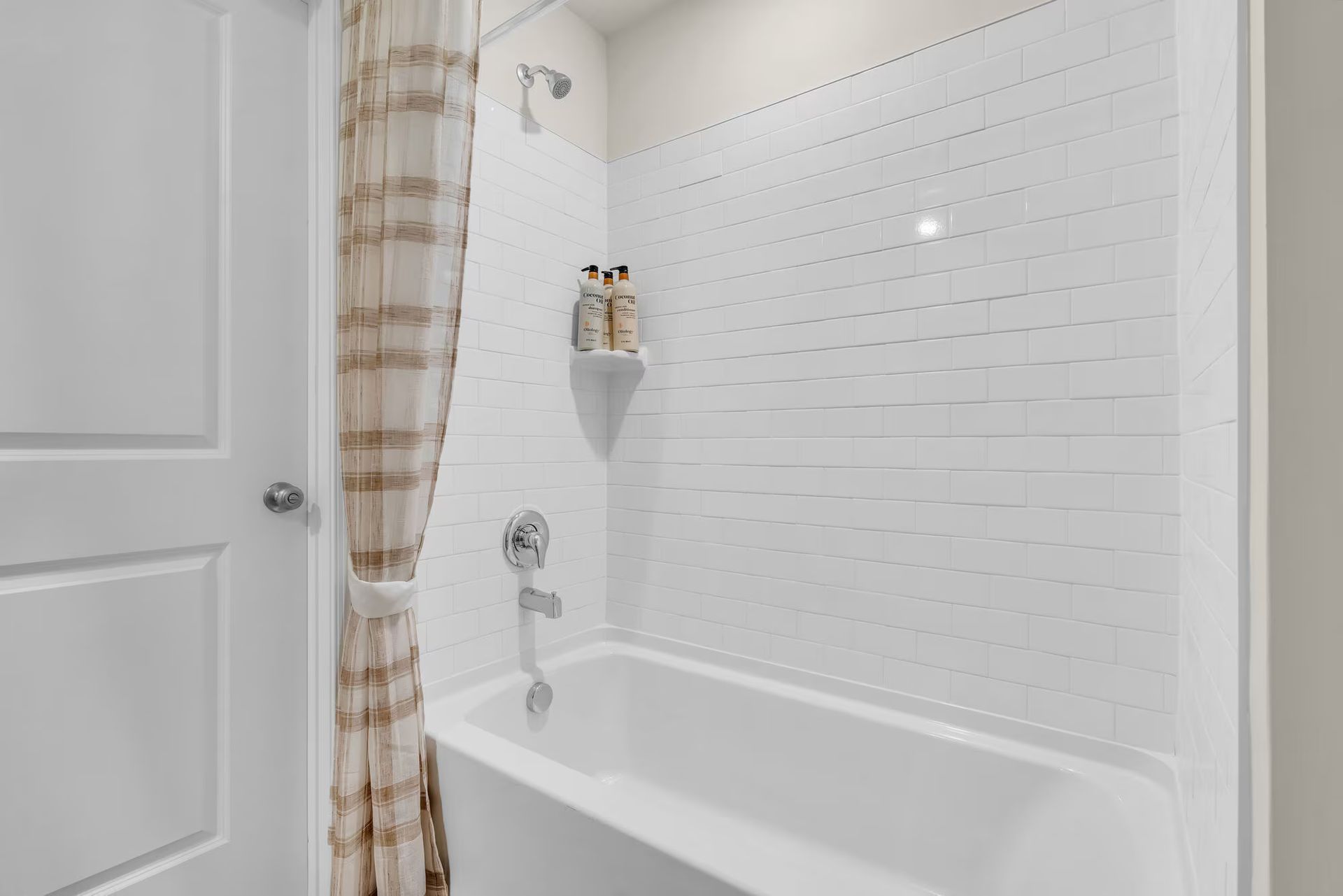 Bright white bathroom with a tiled tub-shower, built-in shelf, and beige plaid shower curtain