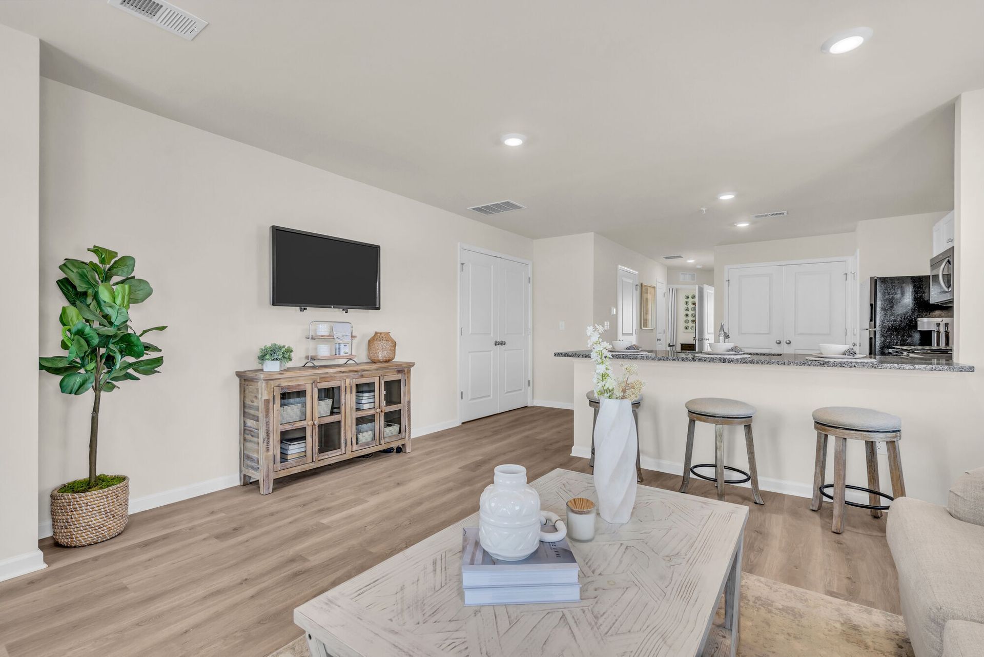 Bright open-concept living room and kitchen with white walls, wood floors, and neutral decor