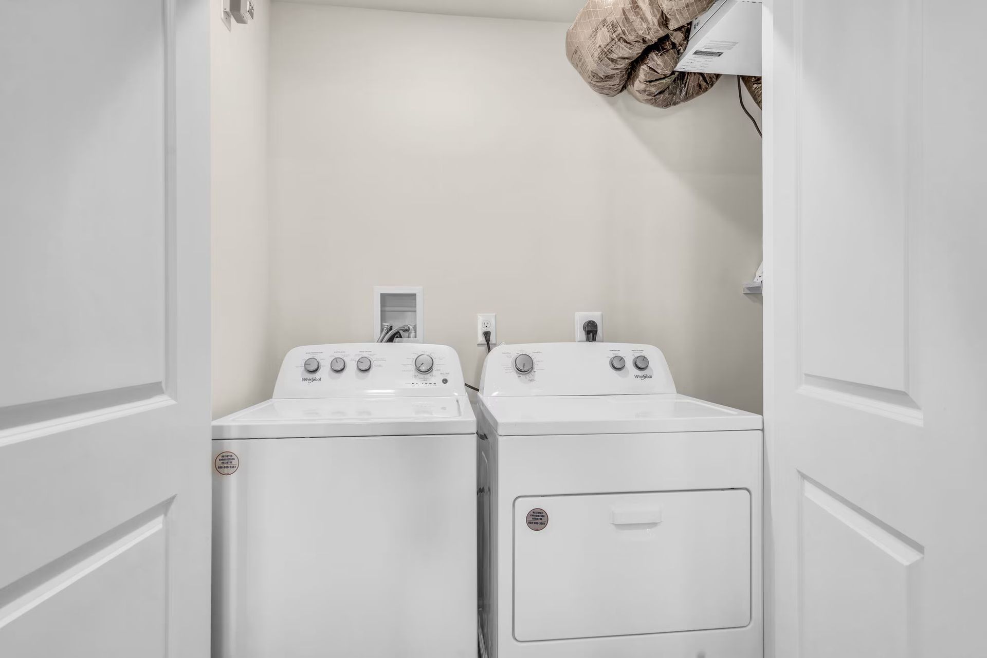 Laundry closet with a white washer and dryer behind open doors