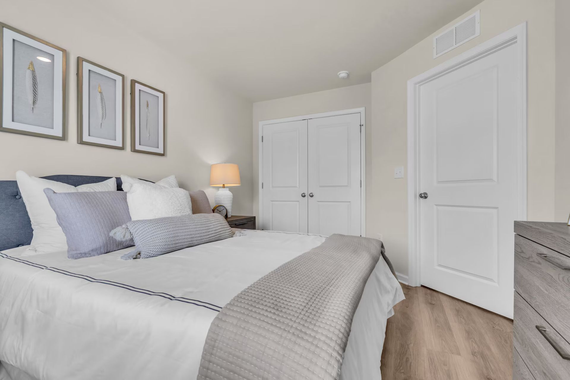 Bright bedroom with a neatly made bed, framed wall art, and white closet and door