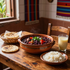 Comida tradicional servida en una mesa de madera: guiso de barro, arroz, tortillas y una bebida en una cocina rústica.
