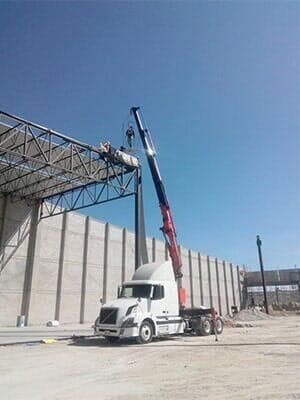 Un camión con una grúa adjunta está estacionado frente a un edificio en construcción.