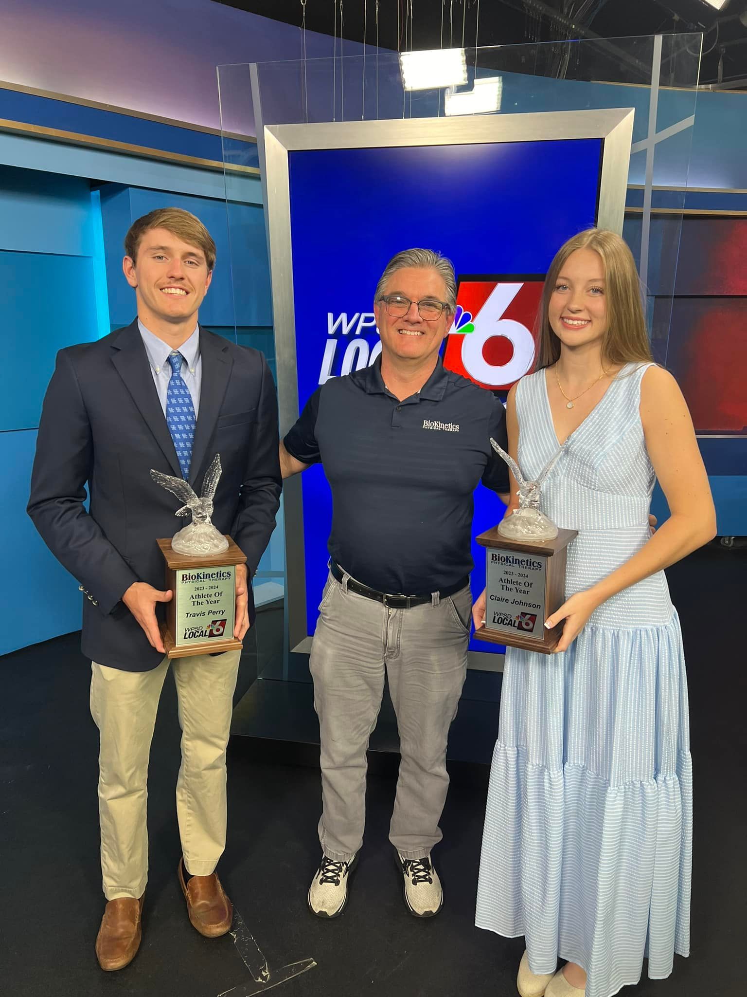 A man and two women are holding trophies in a news studio.