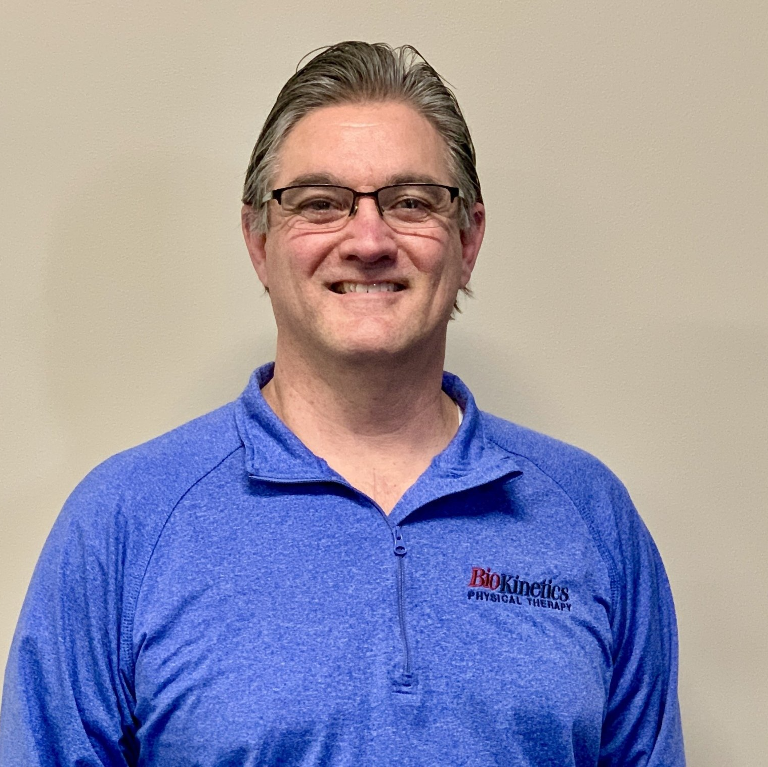 A man wearing glasses and a blue shirt is smiling for the camera.