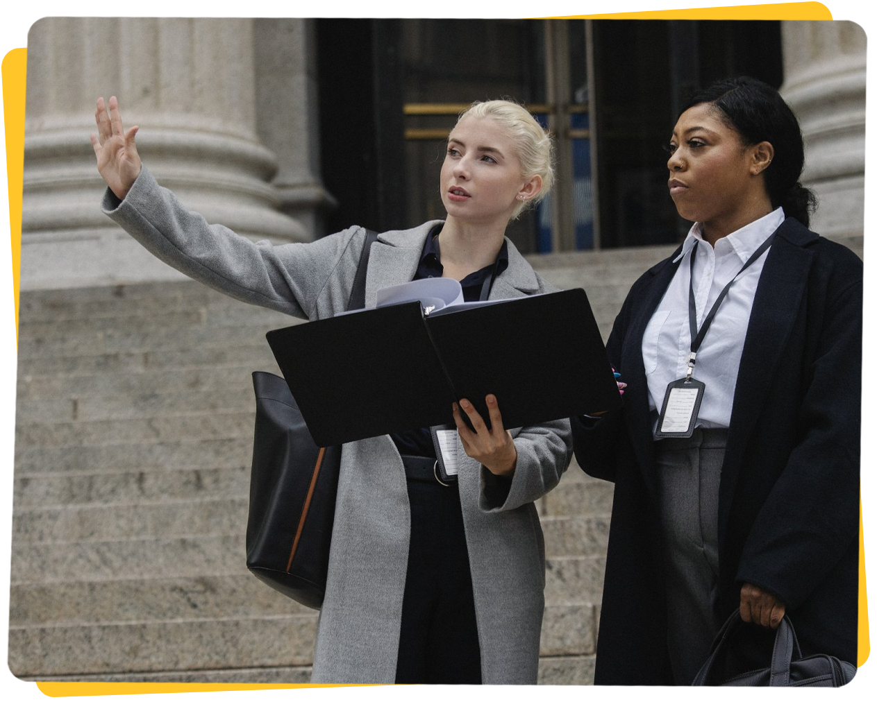 Two people outside a building; one points, holding a folder, the other holds a folder.