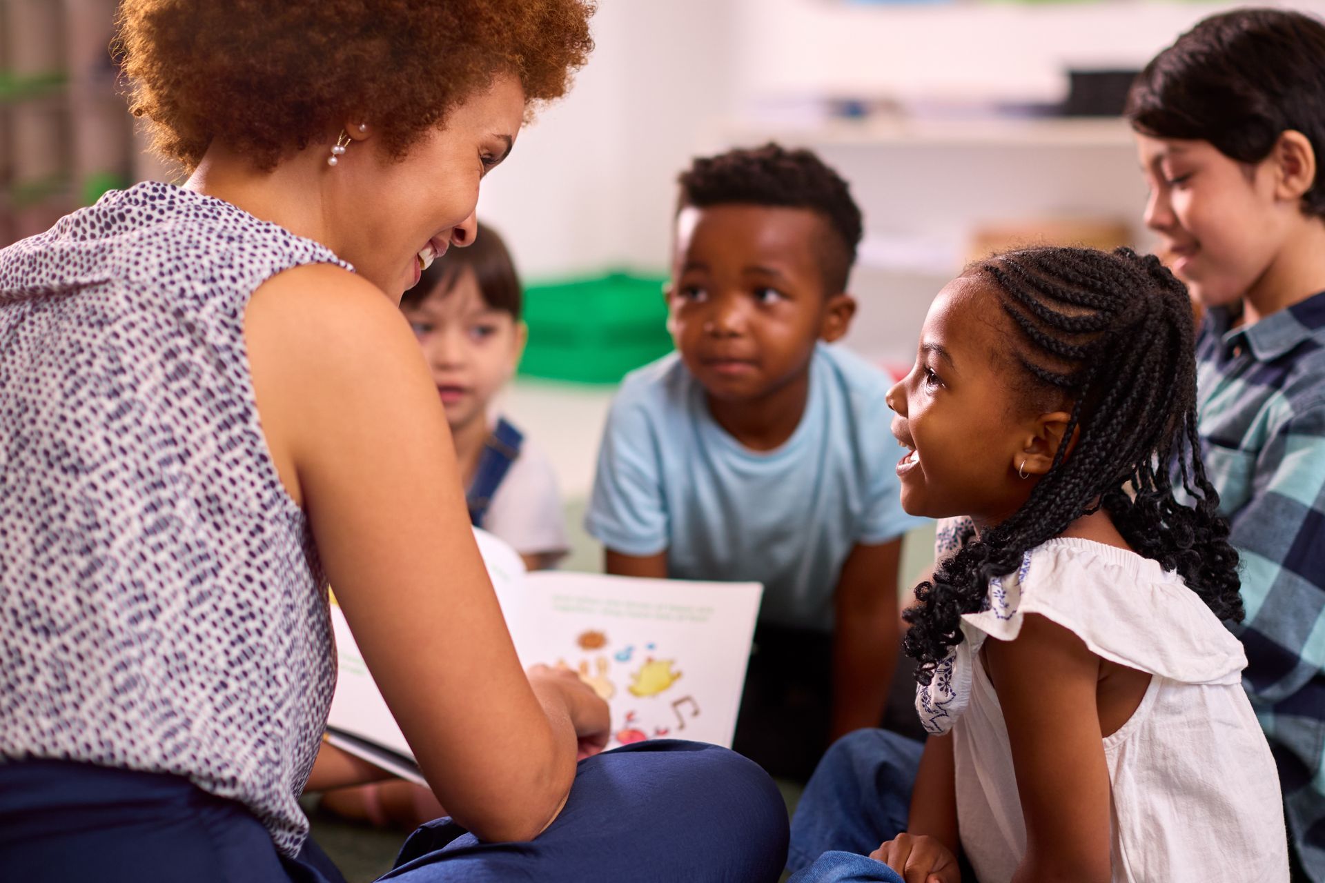 teacher working with children reading book in classroom.