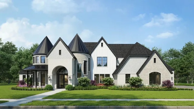 Large white stone house with dark roofs, arched entry, and landscaped front yard under a blue sky