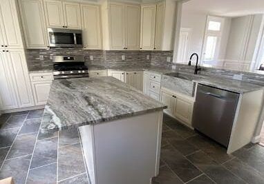 Bright modern kitchen with white cabinets, gray granite island, and stainless steel appliances.