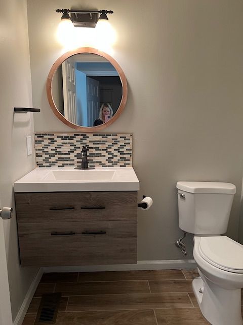 Small bathroom with wood vanity, round mirror, wall light, and white toilet.