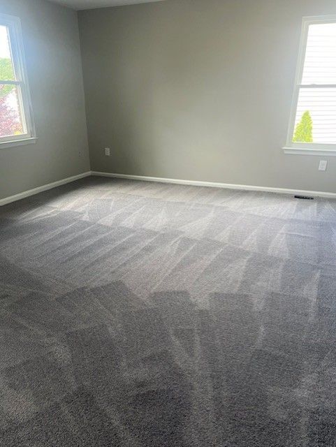 Empty gray carpeted room with light gray walls and two windows letting in daylight