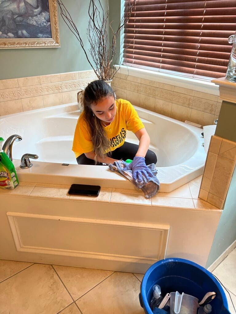 Person cleaning a white bathtub with a purple cloth in a bathroom.