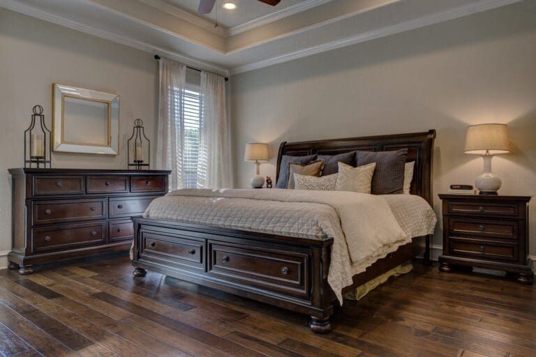 Spacious bedroom with dark wood bed, matching dresser, bedside tables, and warm lighting