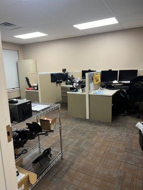 Office workspace with desks, computers, and a metal shelving cart in a carpeted room.