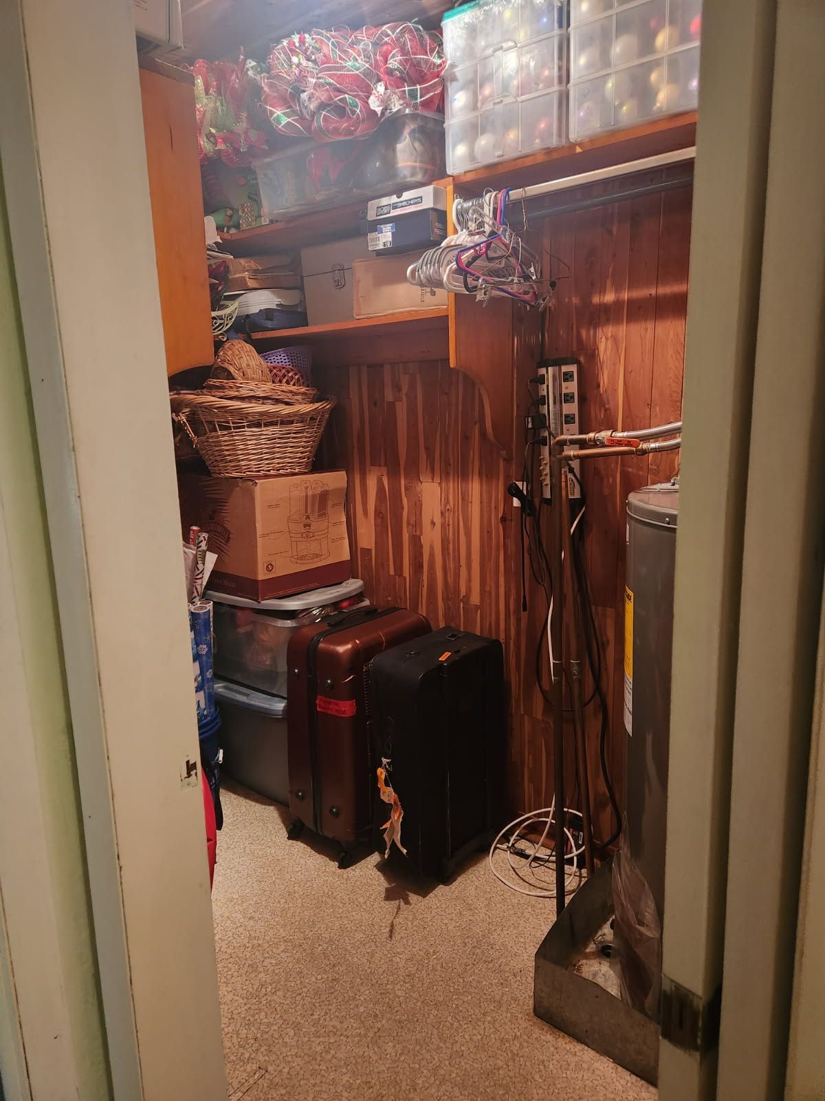 A narrow closet with shelves of baskets, boxes, cords, and a black speaker on the carpet.