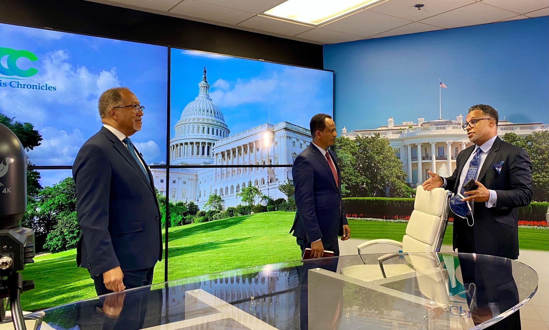 Three men in suits are standing in front of a large screen.