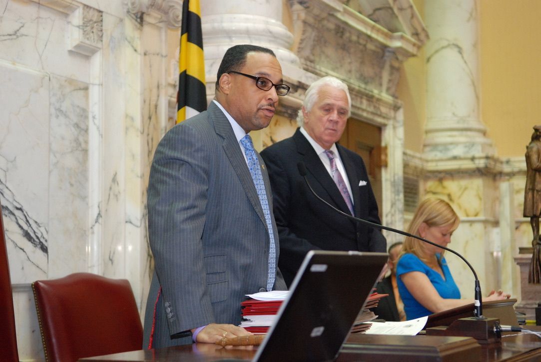 A man in a suit and tie is standing next to another man in front of a microphone.