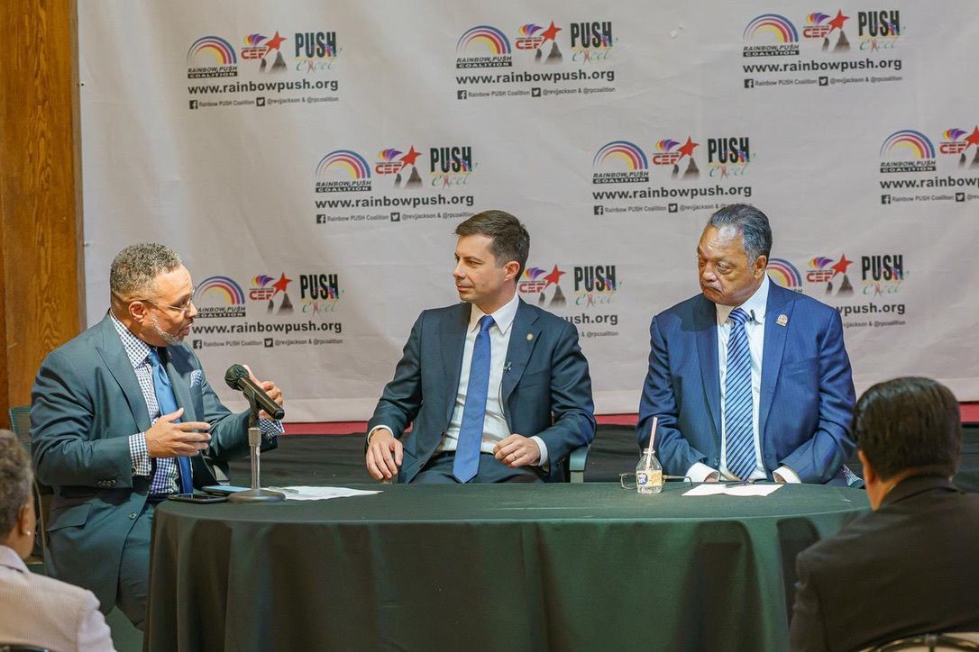 Three men in suits and ties are sitting at a table talking into microphones.
