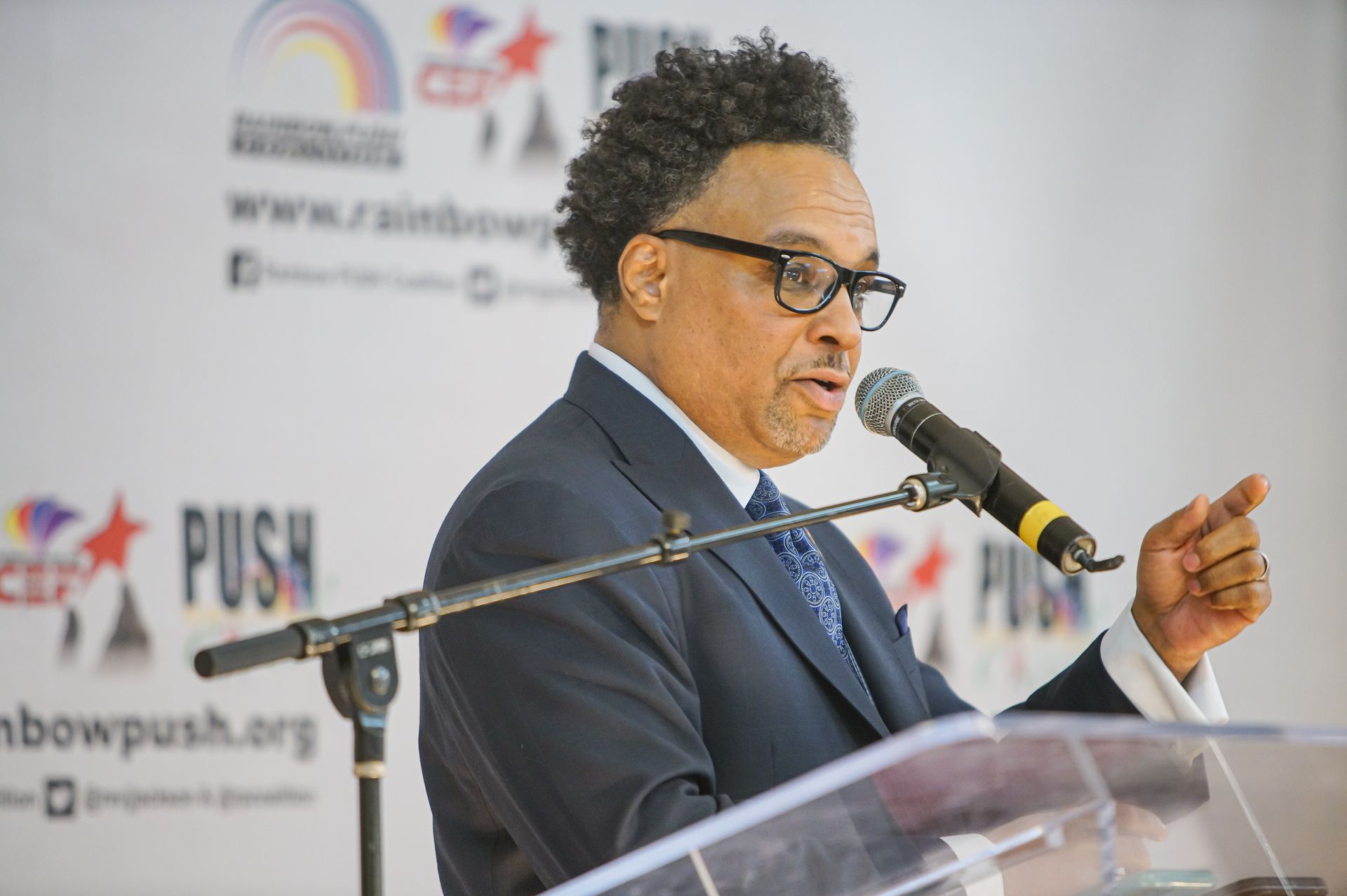A man in a suit and tie is speaking into a microphone.