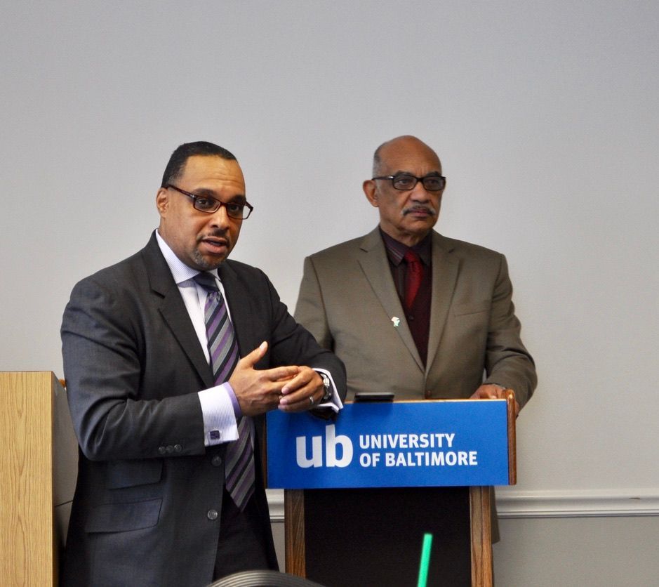 Two men standing behind a podium that says university of baltimore