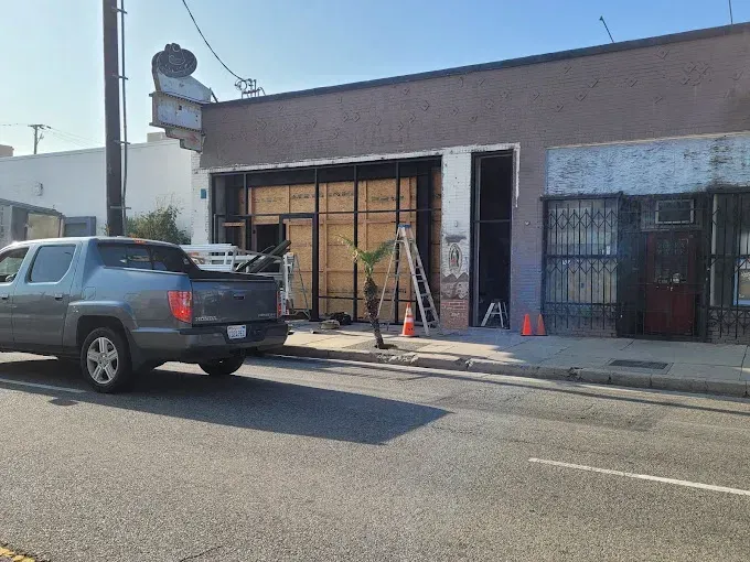 Street view of a storefront under construction with a parked gray SUV and traffic cones