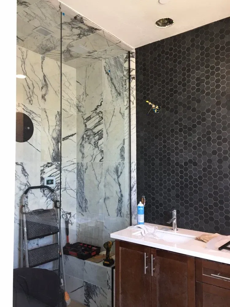 Modern bathroom with glass shower, marble walls, dark tile accent, and vanity sink