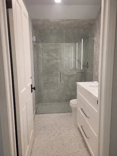 Small bathroom with glass-enclosed shower, white vanity, and open door.