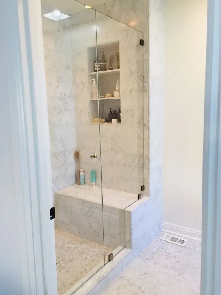 Glass shower enclosure with built-in shelf and marble-style tile in a bright bathroom
