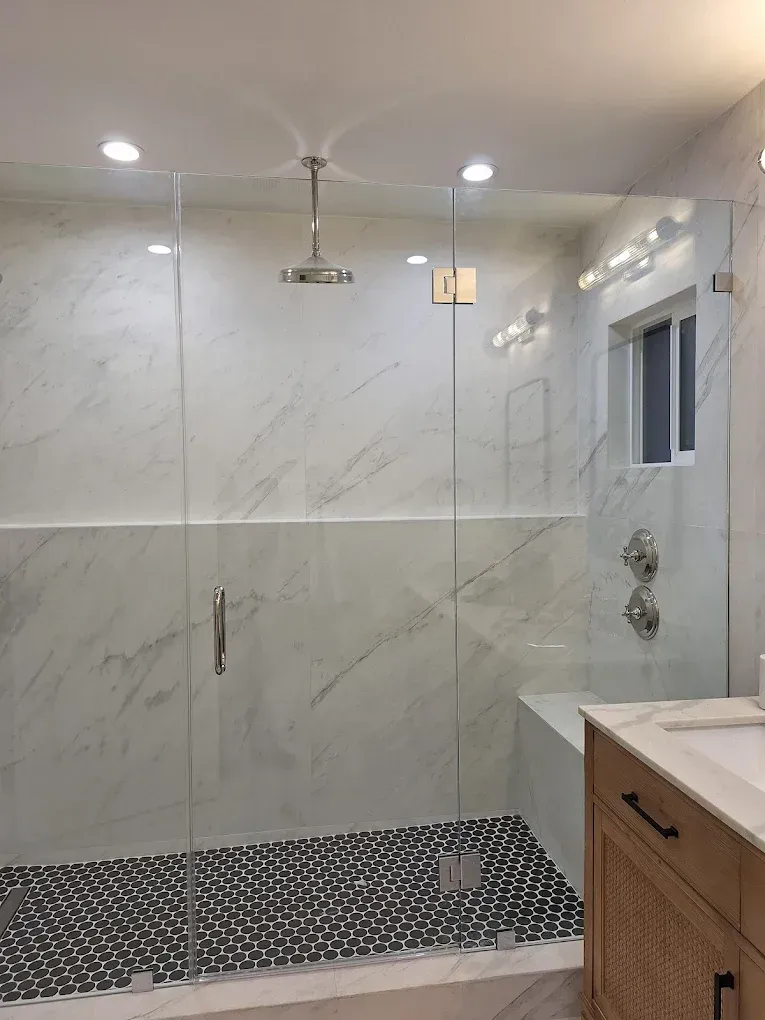 Modern bathroom with glass shower enclosure, black pebble floor, marble-look walls, and window.