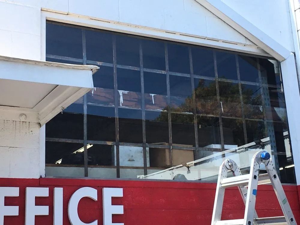 Storefront window with red “OFFICE” sign and a ladder leaning against the building