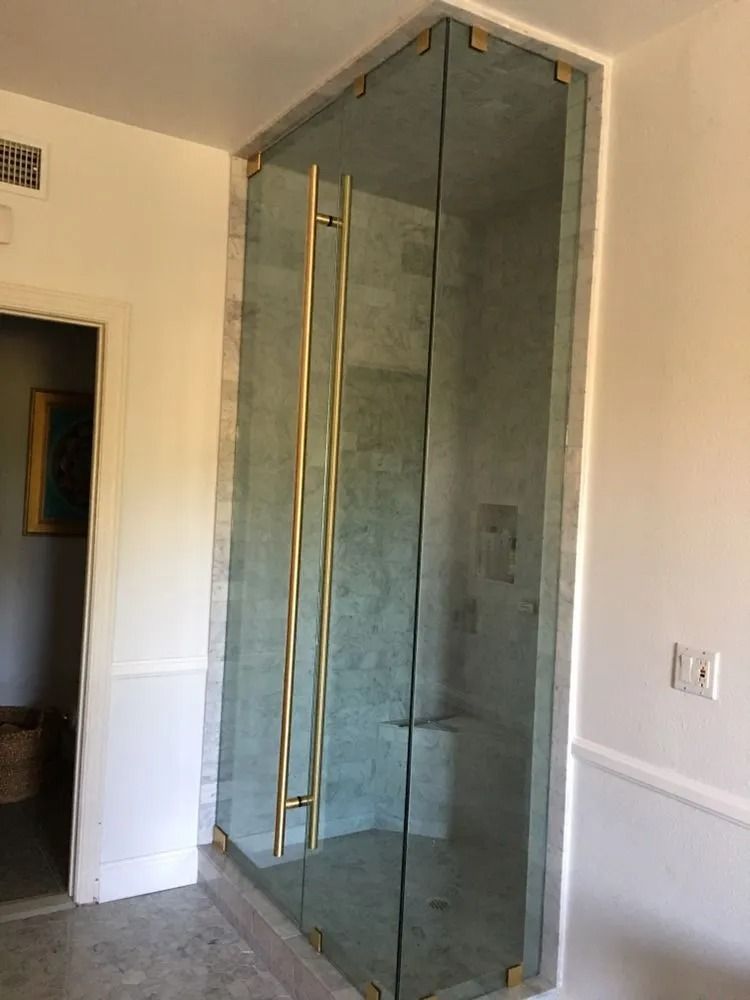 Modern bathroom with a glass-enclosed shower and gold hardware beside a doorway