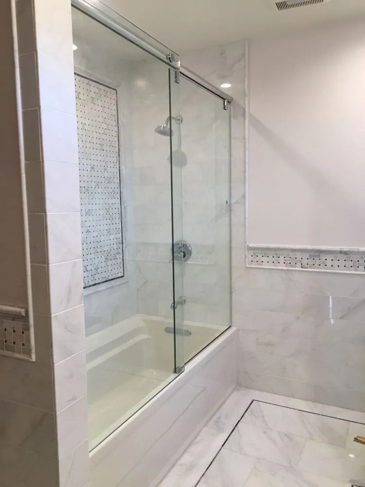 Bathroom with a glass-enclosed bathtub shower, white tile walls, and a tiled floor.