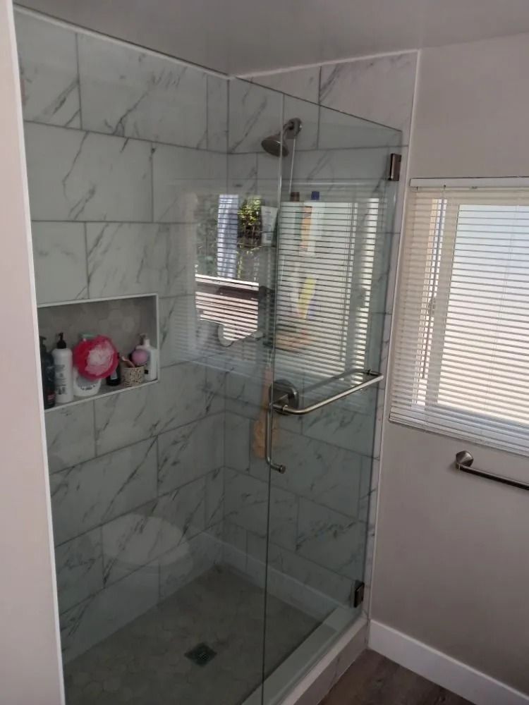 Modern bathroom with glass shower, marble tile walls, and a window with blinds.