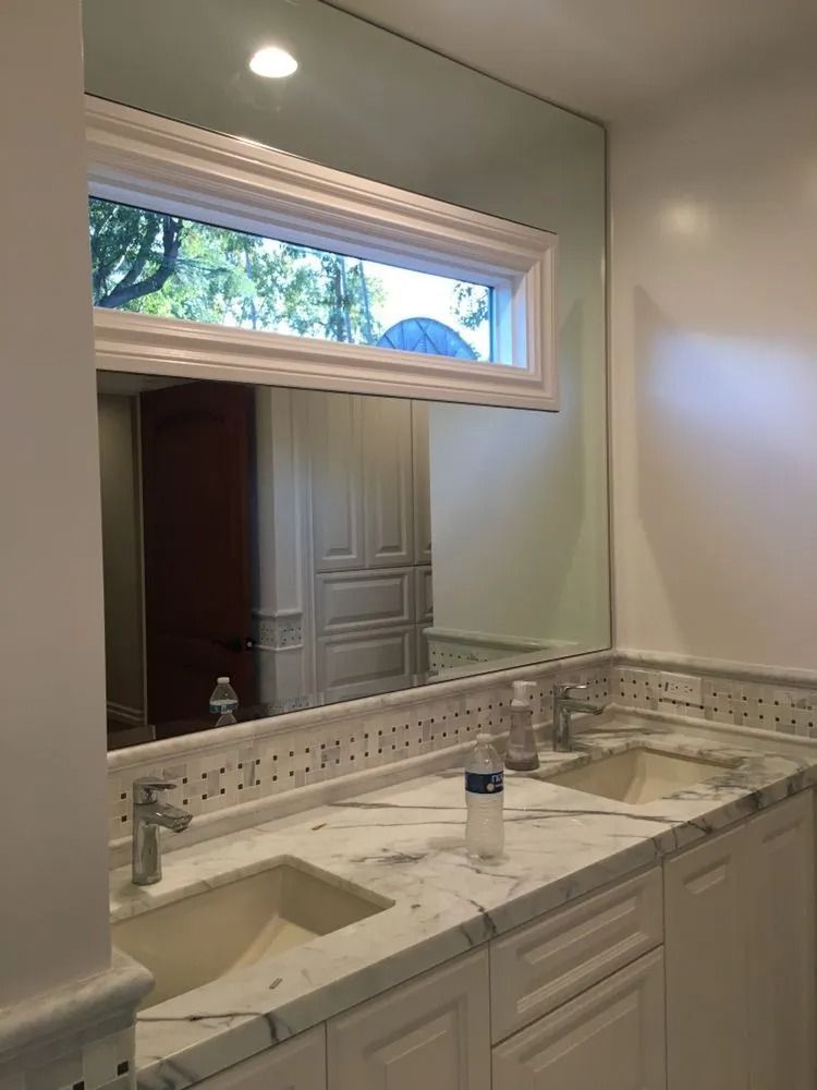 Bright bathroom vanity with marble countertop, double sinks, large mirror, and window above the mirror.