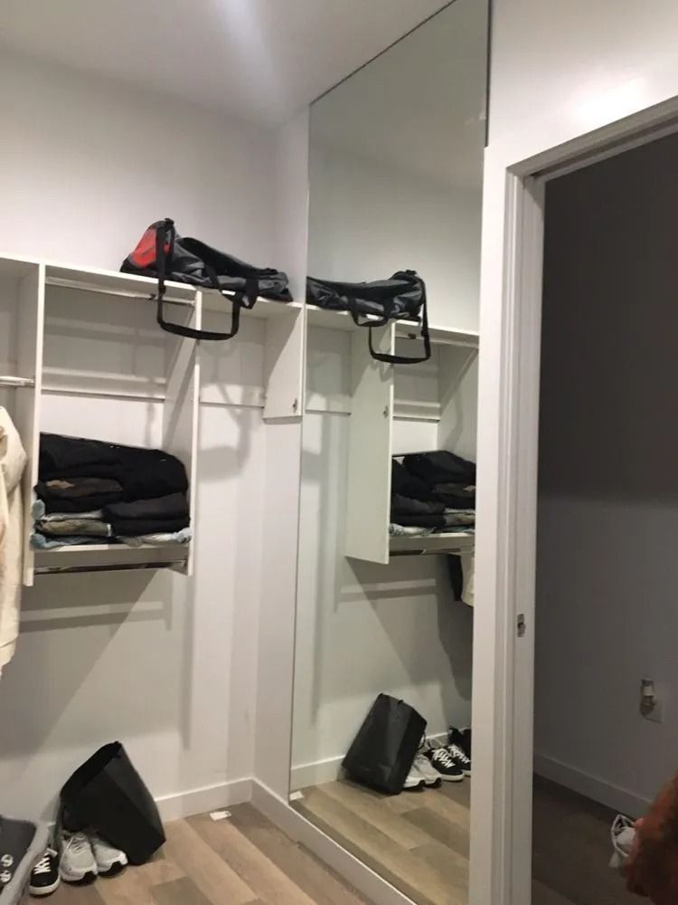Open closet with shelves, hanging clothes, and a large mirror reflecting the room.