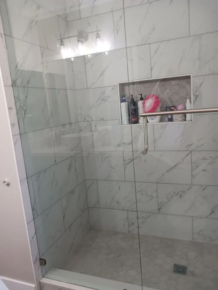 Tiled walk-in shower with a built-in shelf holding toiletries and a glass partition.