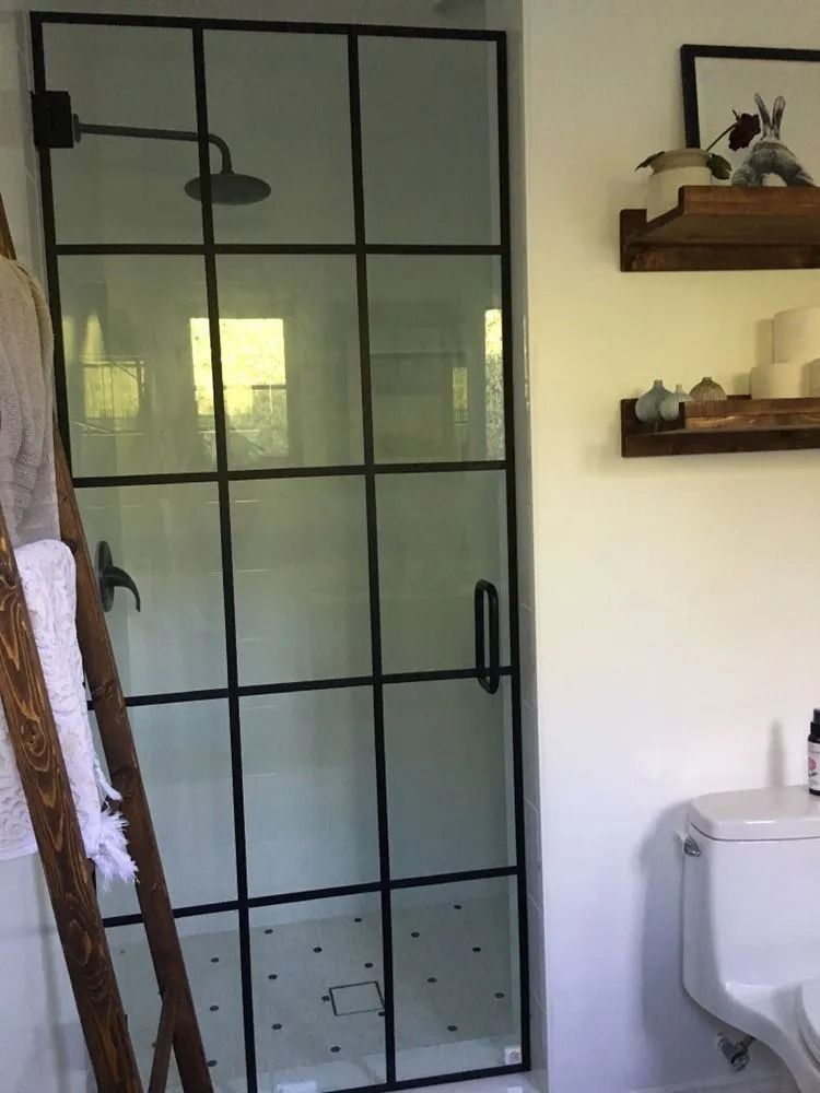 Black-framed glass shower enclosure in a bathroom, with wall shelves and a toilet beside it.
